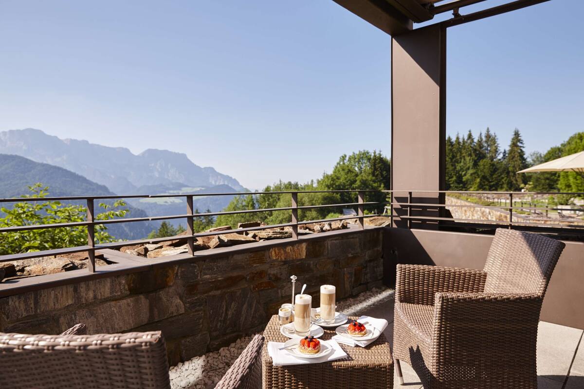 Een terras met rieten meubilair, een tafel gedekt met borden, kaarsen en uitzicht op bergen.