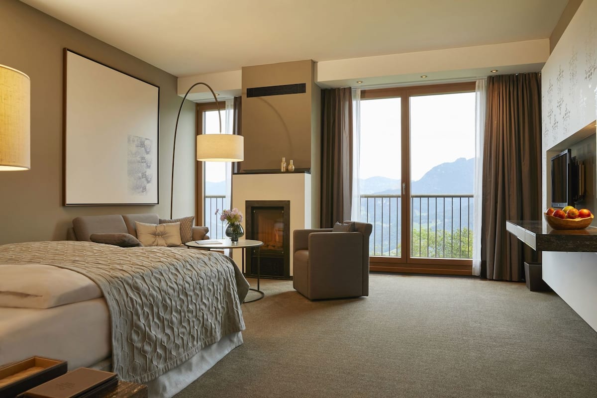 Een hotelkamer met een bed, zithoek, open haard, televisie en een balkon met uitzicht op de bergen.