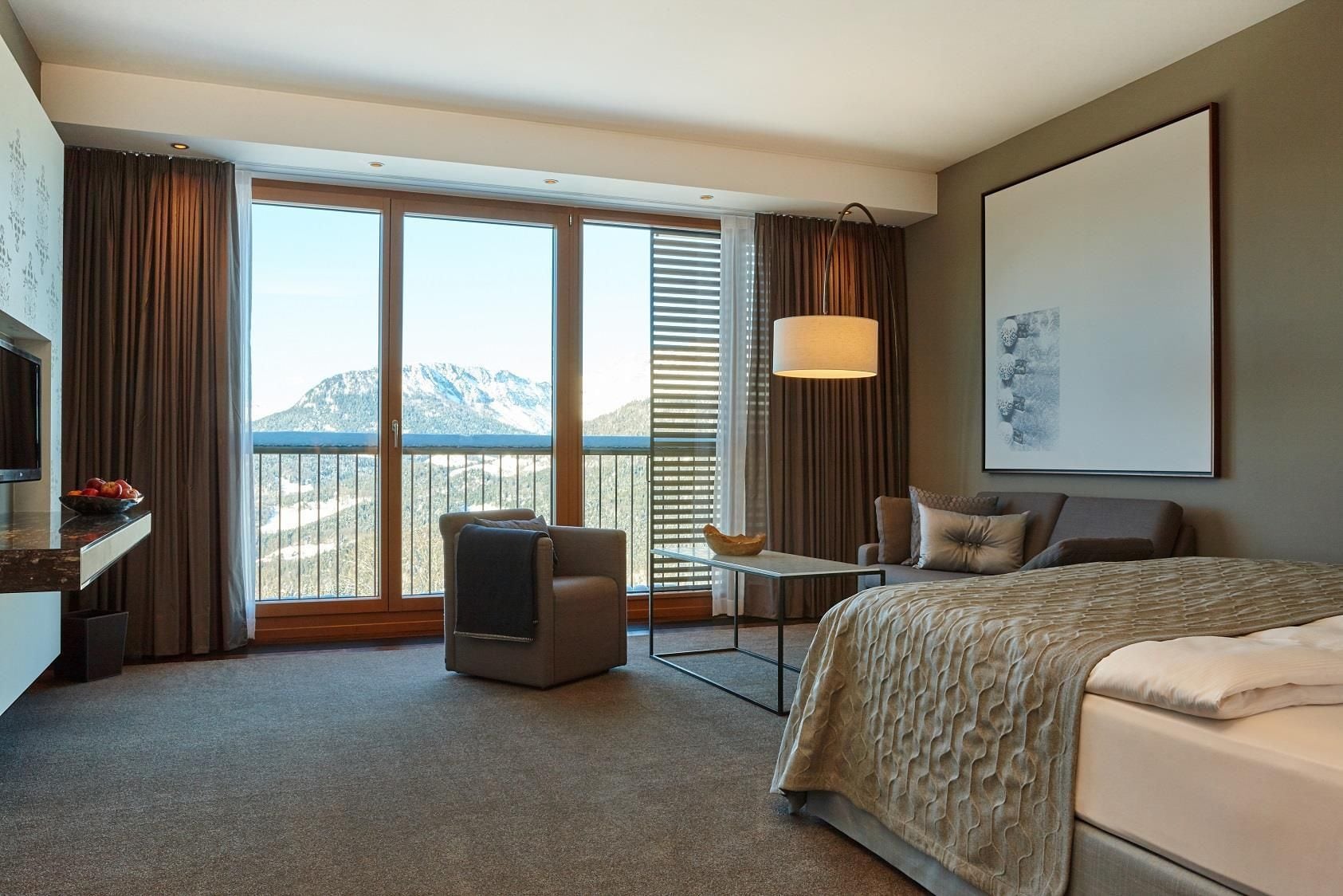 Habitación de hotel con cama, escritorio, silla, televisor y una ventana grande con vista a la montaña.