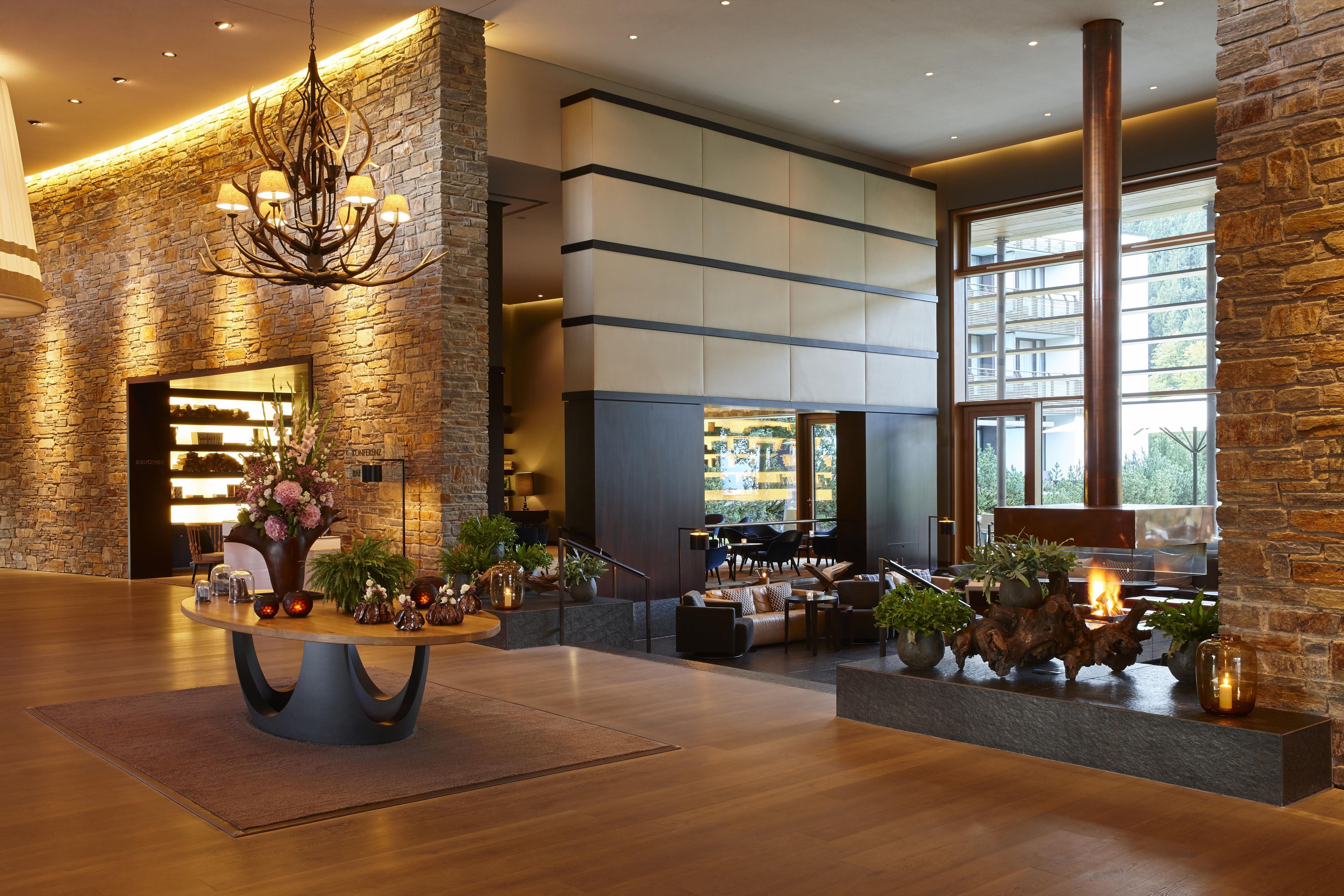 A modern lobby with a stone wall, a chandelier, and a seating area with a fireplace.