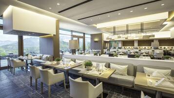 A modern restaurant with high ceilings, large windows, and a view of mountains.