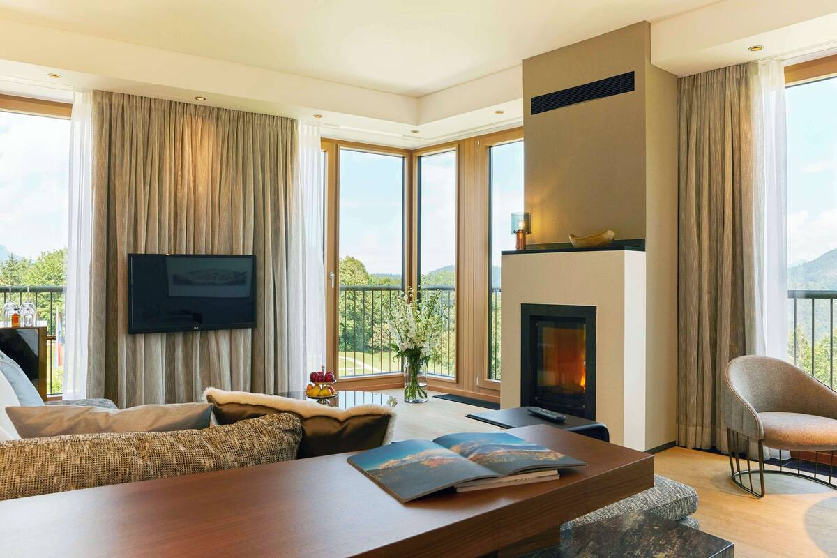 Een moderne woonkamer met een open haard, grote ramen en een flatscreen televisie.
