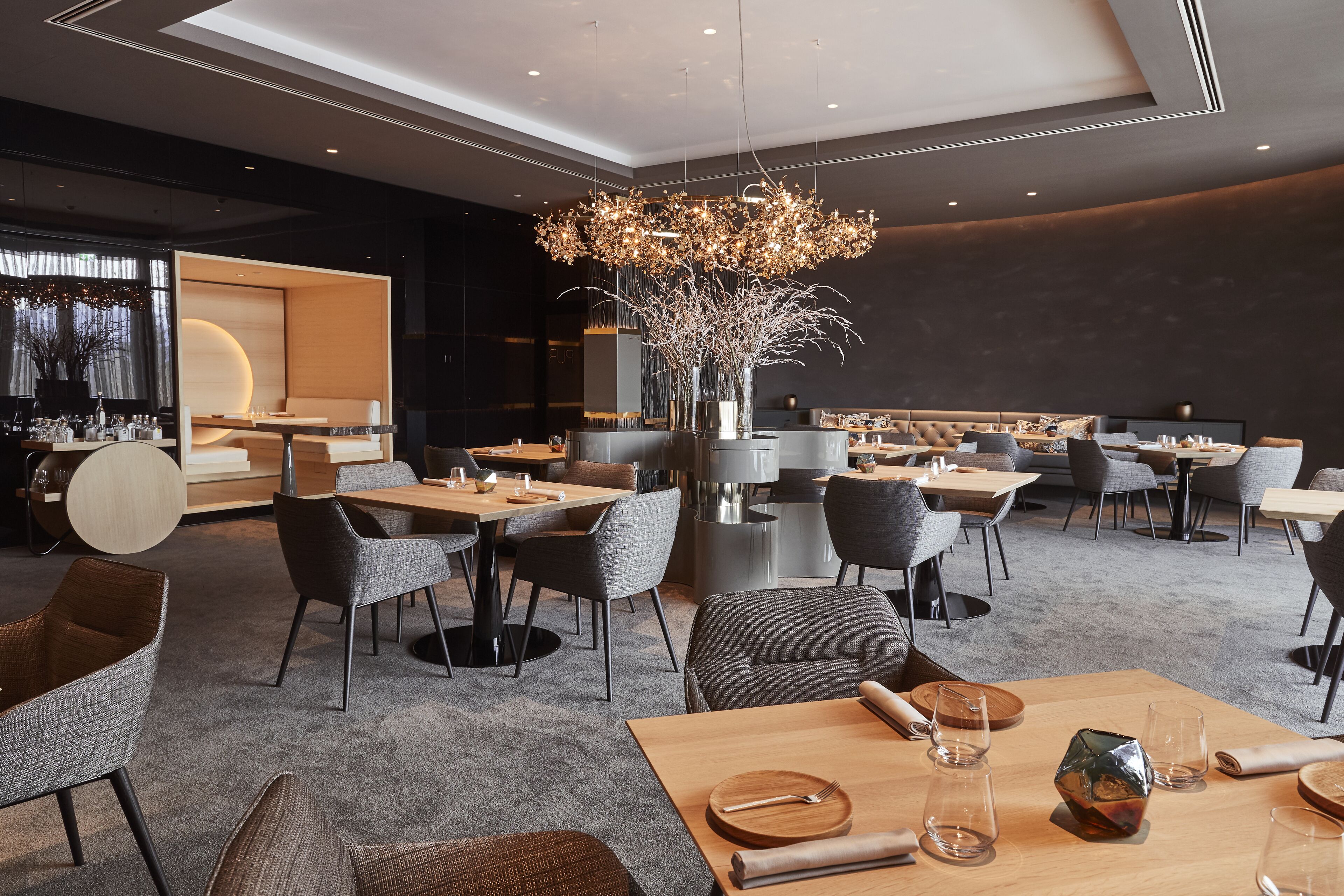 A modern dining area with multiple tables and chairs, a central decorative light fixture, and a large vase with branches.