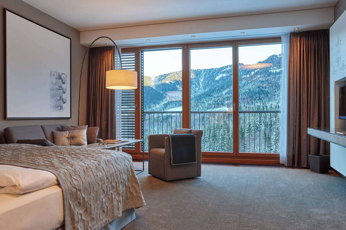 Een hotelkamer met een groot bed, een televisie, een bureau en een balkon met uitzicht op de bergen.