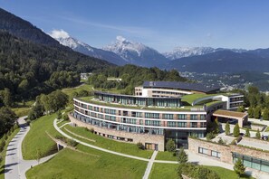 Un edificio moderno con un design curvo, immerso nel verde e con montagne sullo sfondo.