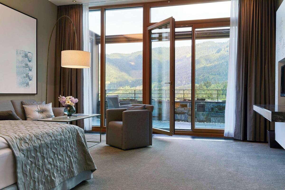 Hotelkamer met een groot bed, een zithoek met een tafel en stoelen, een televisie, en een balkon met uitzicht op de bergen.