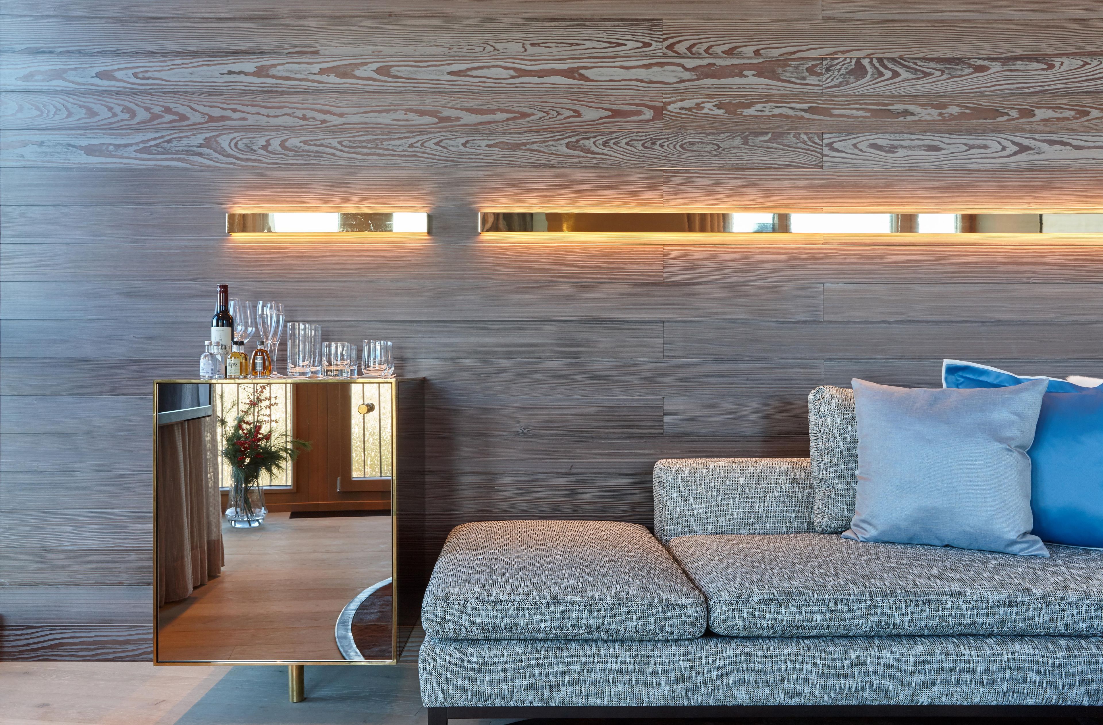 A modern living room with a patterned sofa, a mirrored cabinet, and a wall-mounted light fixture.