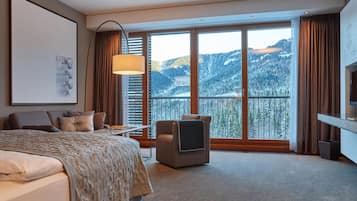 Habitación de hotel con cama, escritorio, silla, televisión y un amplio ventanal con vista a la montaña.