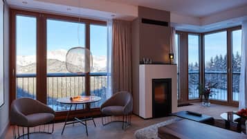 Ein modernes Wohnzimmer mit großen Fenstern, einem Kamin und einem Balkon mit Blick auf verschneite Berge.
