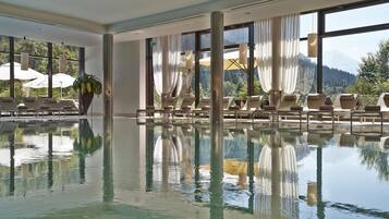 Una piscina interior con agua cristalina, tumbonas y vistas a montañas a través de amplios ventanales.