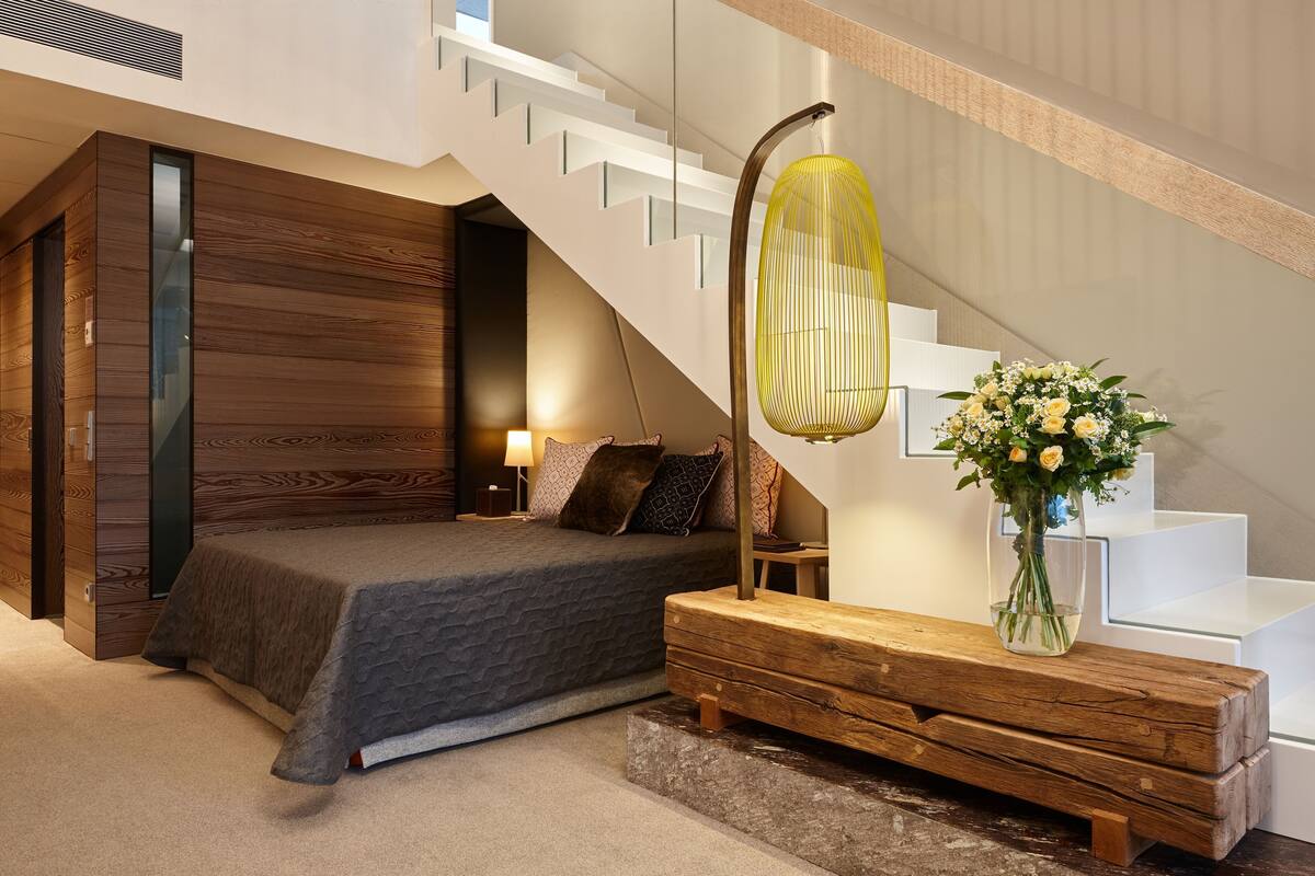 Een slaapkamer met een bed, nachtkastje, lamp en een bloemenvaas.