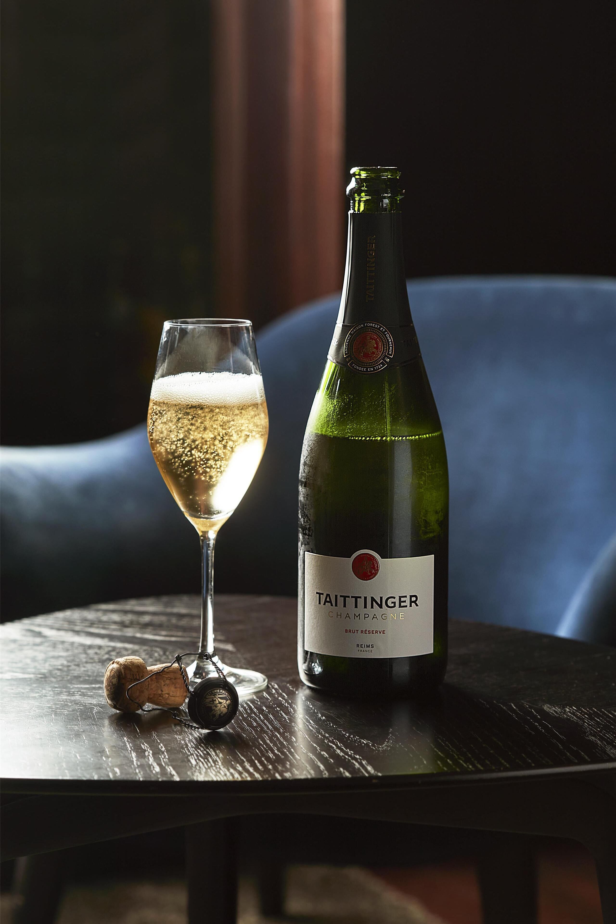 Eine Flasche Taittinger Champagner und ein Glas mit Bläschen auf einer Holztisch.