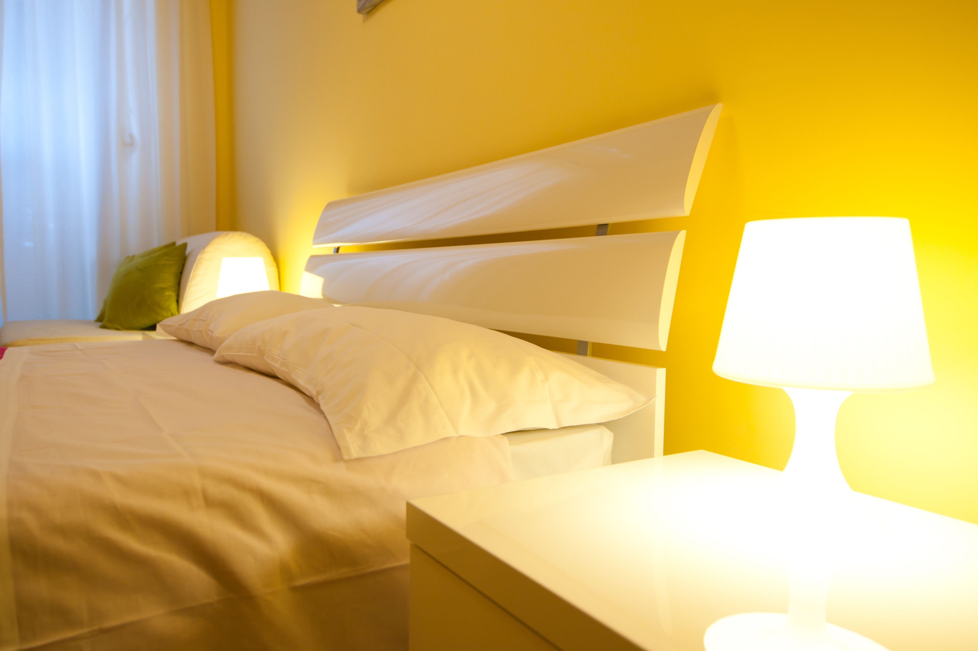 A hotel room with a bed, a nightstand, and a lamp.