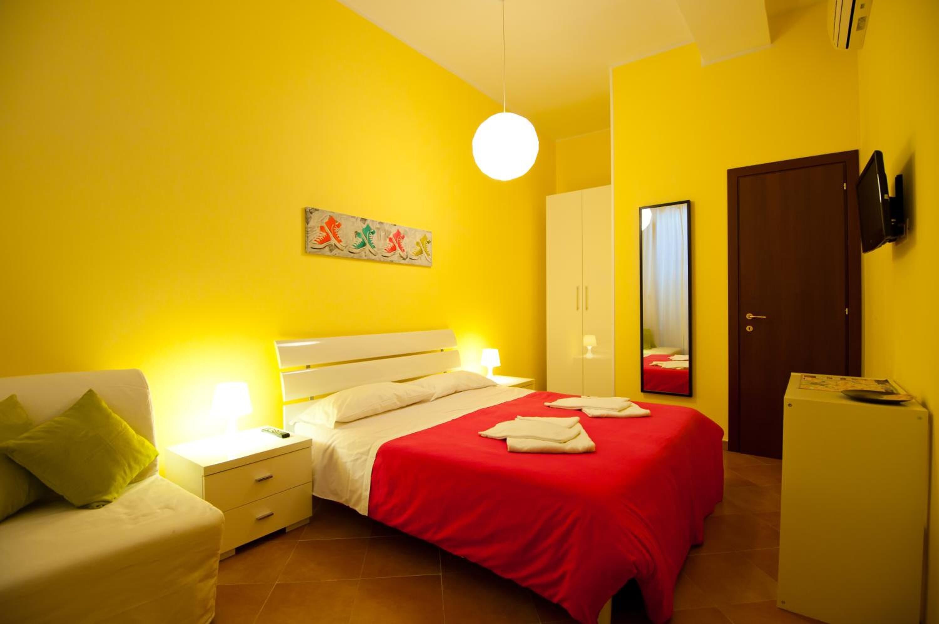 Une chambre d’hôtel comprenant un lit, une table de chevet, une chaise, une armoire, un miroir, une télévision et un réfrigérateur.