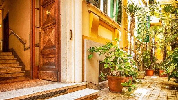 A building entrance with a wooden door, a staircase, and potted plants on a tiled patio. - Domina Popolo B&B (Rome)