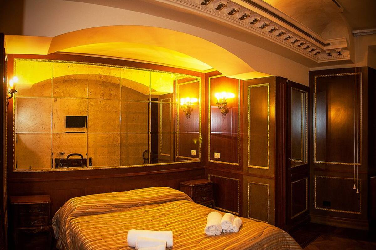 A hotel room with a large mirror, a bed with striped bedding, and a wooden wardrobe.