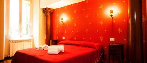 A hotel room with a large bed, two bedside tables, a window, and a red wall with a floral pattern.