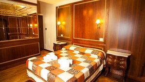 A hotel room with a large bed, wooden paneling, a mirror, two wall-mounted lamps, and a small wooden nightstand. - Domina Popolo B&B (Rome)