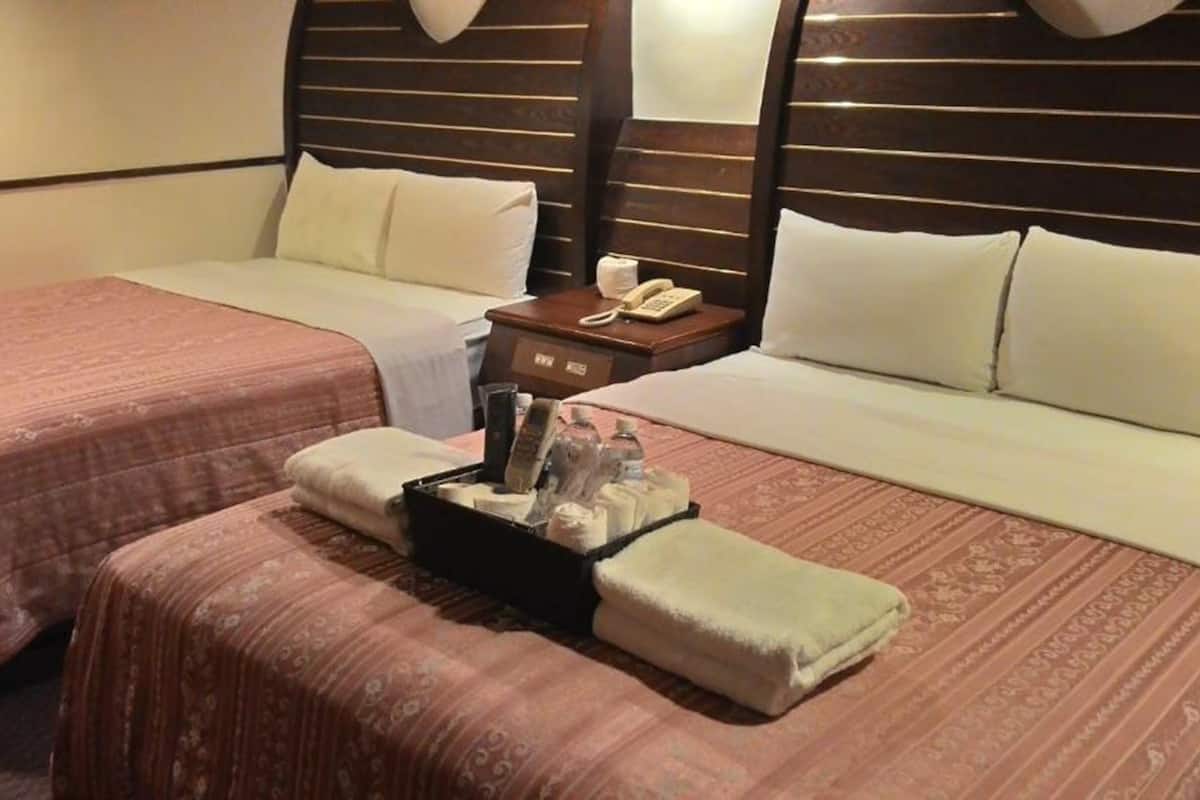 A hotel room with two beds, a bedside table with a phone, and a tray with toiletries.