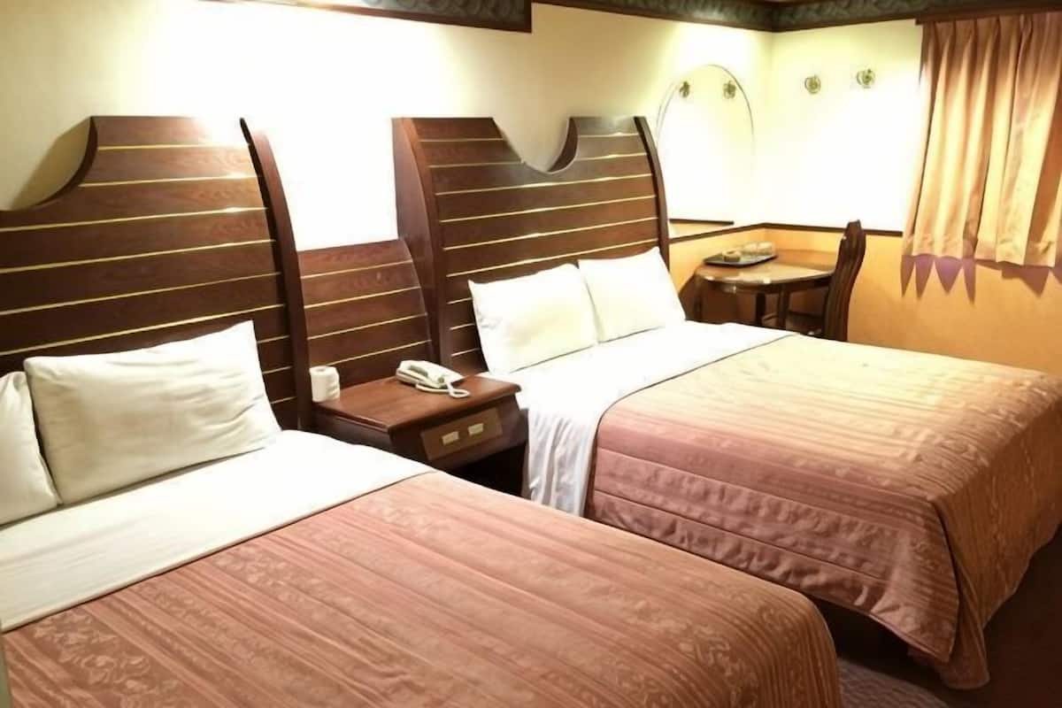 A hotel room with two beds, a bedside table with a phone, and a small table with a lamp.