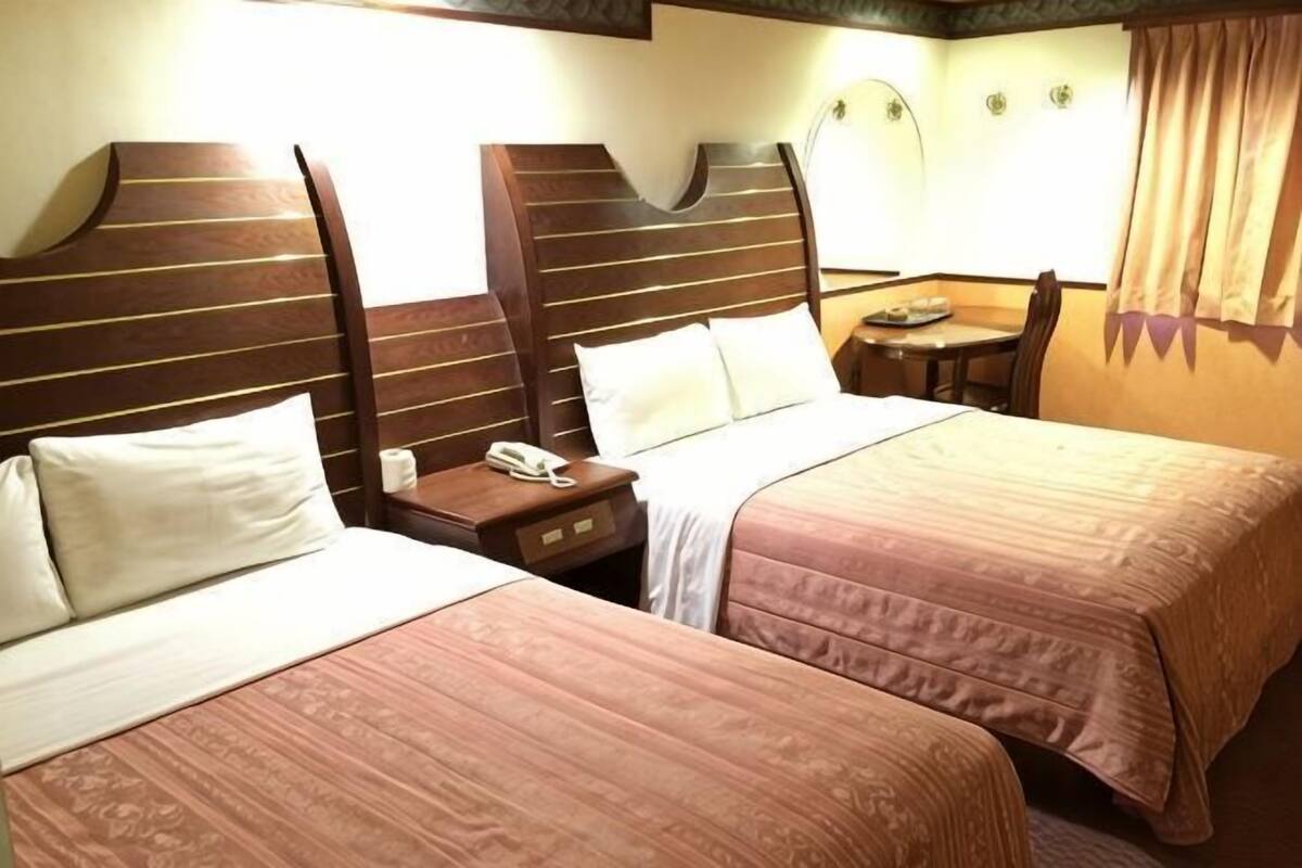 Ein Hotelzimmer mit zwei Betten, einem Nachttisch mit Telefon und einem kleinen Tisch mit Lampe.