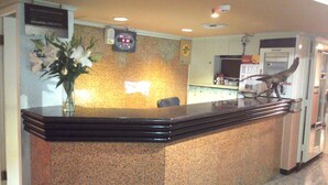 Un mostrador de recepción con un reloj digital, un jarrón con flores y una estatua.