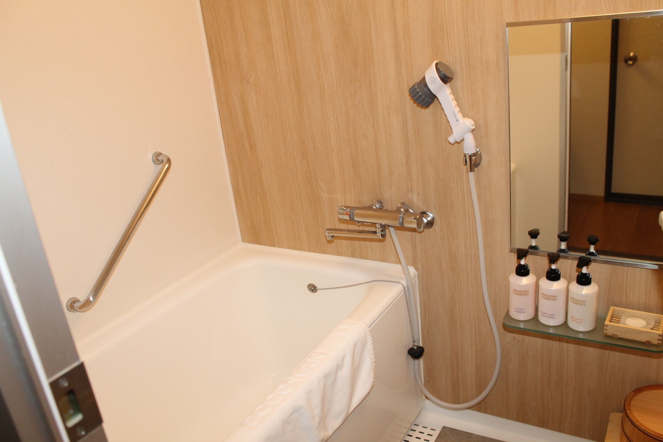 A bathroom with a bathtub, a handrail, a showerhead, and a shelf with toiletries.