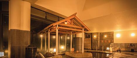 A traditional Japanese onsen with stone baths, wooden structures, and ambient lighting.