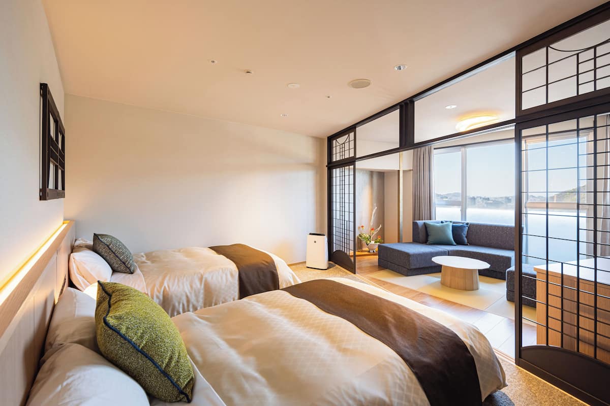 Ein modernes Hotelzimmer mit zwei Betten, einer Sitzecke, einem kleinen Tisch und großen Fenstern mit Blick.