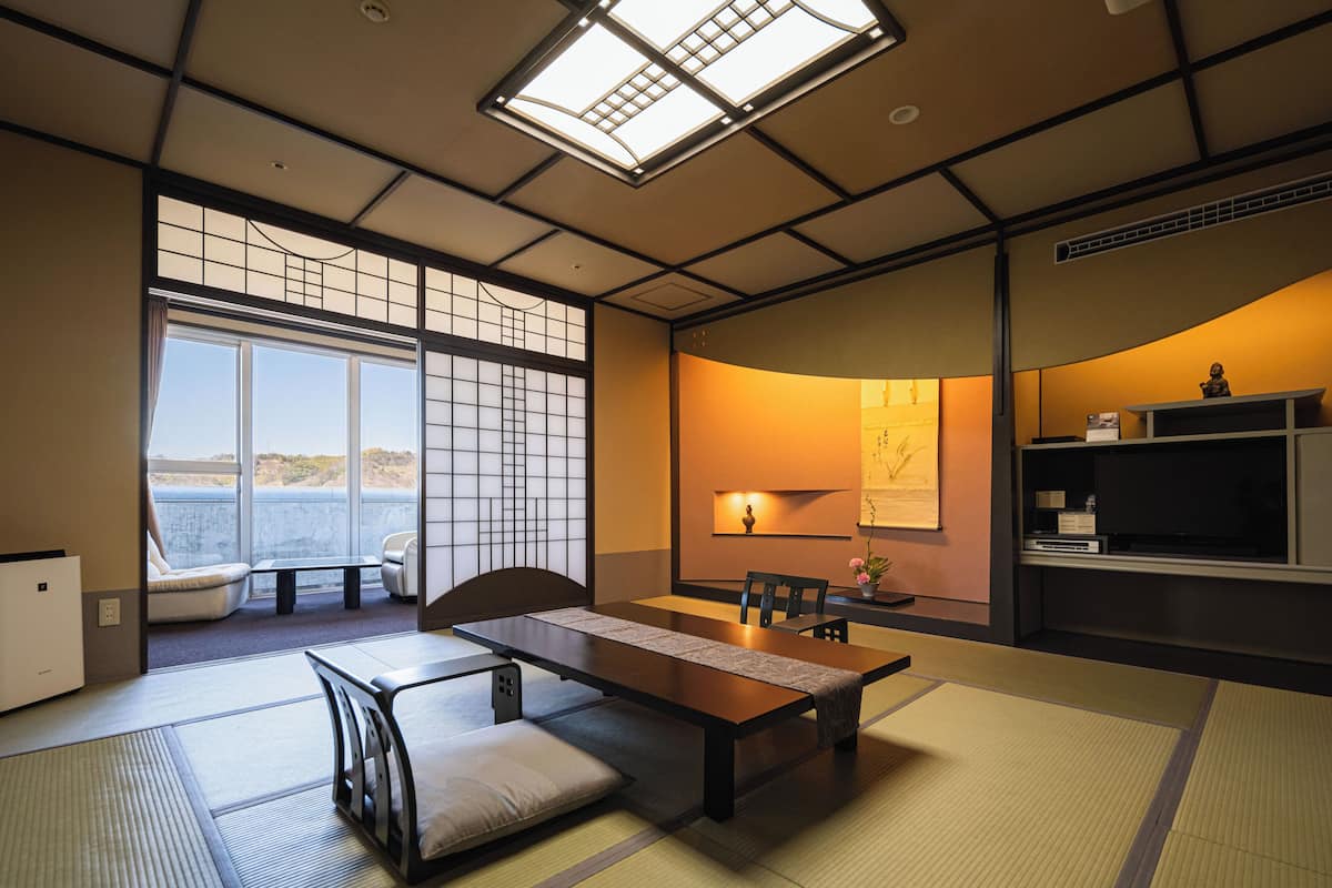 Ein traditioneller japanischer Raum mit Tatami-Böden, einem niedrigen Tisch, Stühlen, einer Schiebetür und Blick auf das Meer.