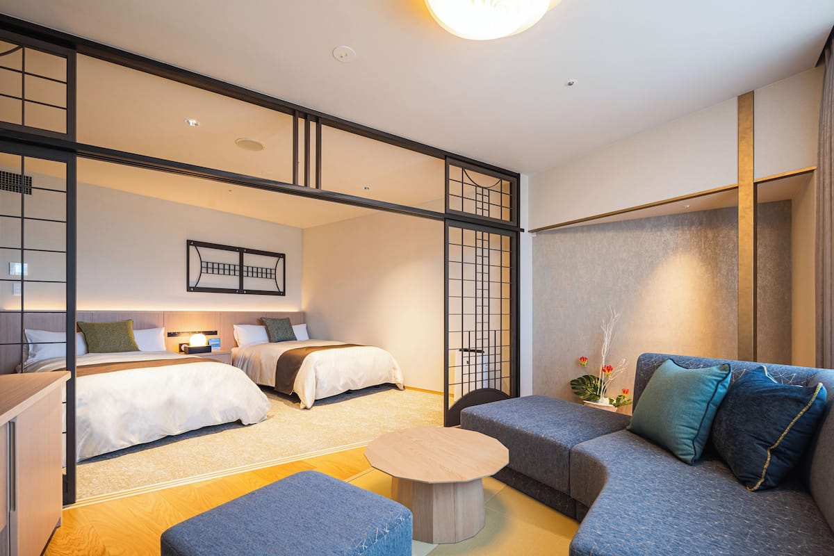 Ein modernes Hotelzimmer mit zwei Betten, einer Couch, einem kleinen Tisch und einem dekorativen Raumteiler.