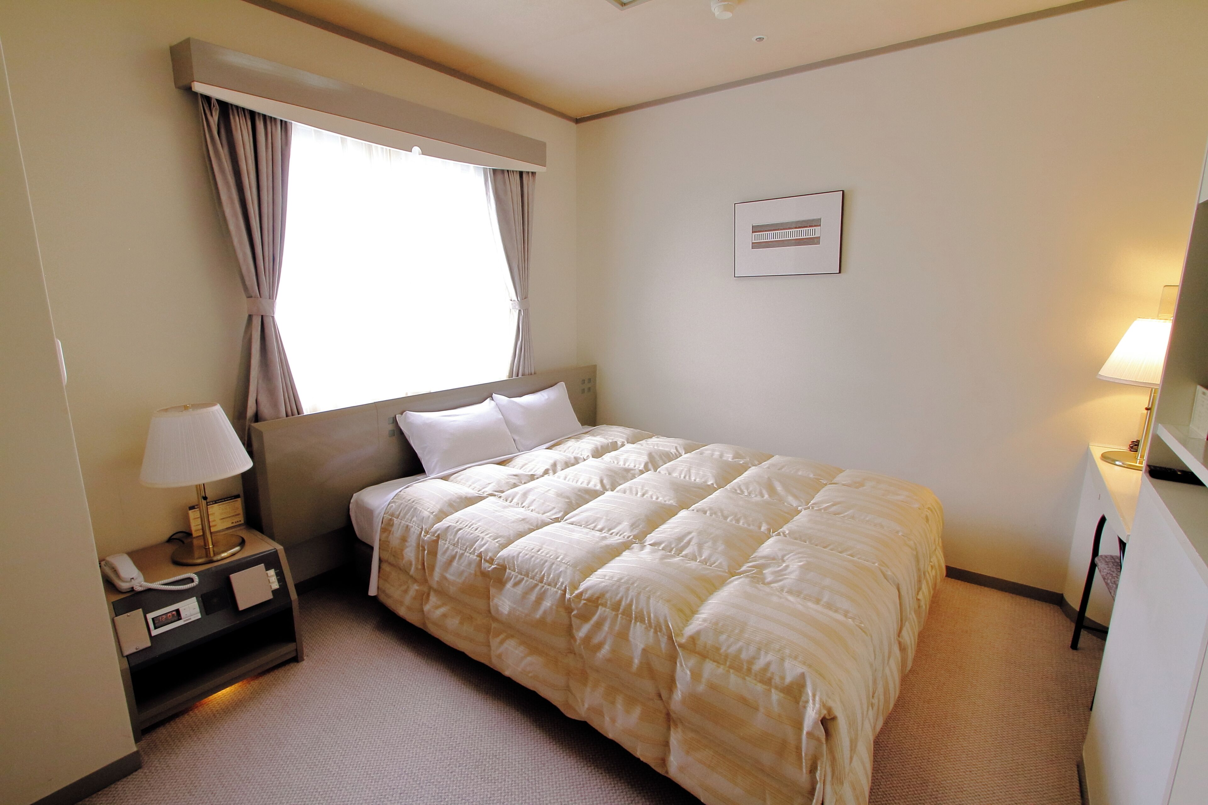 Una habitación de hotel con una cama, una mesita de noche con lámpara, una ventana con cortinas y un aire acondicionado instalado en la pared.