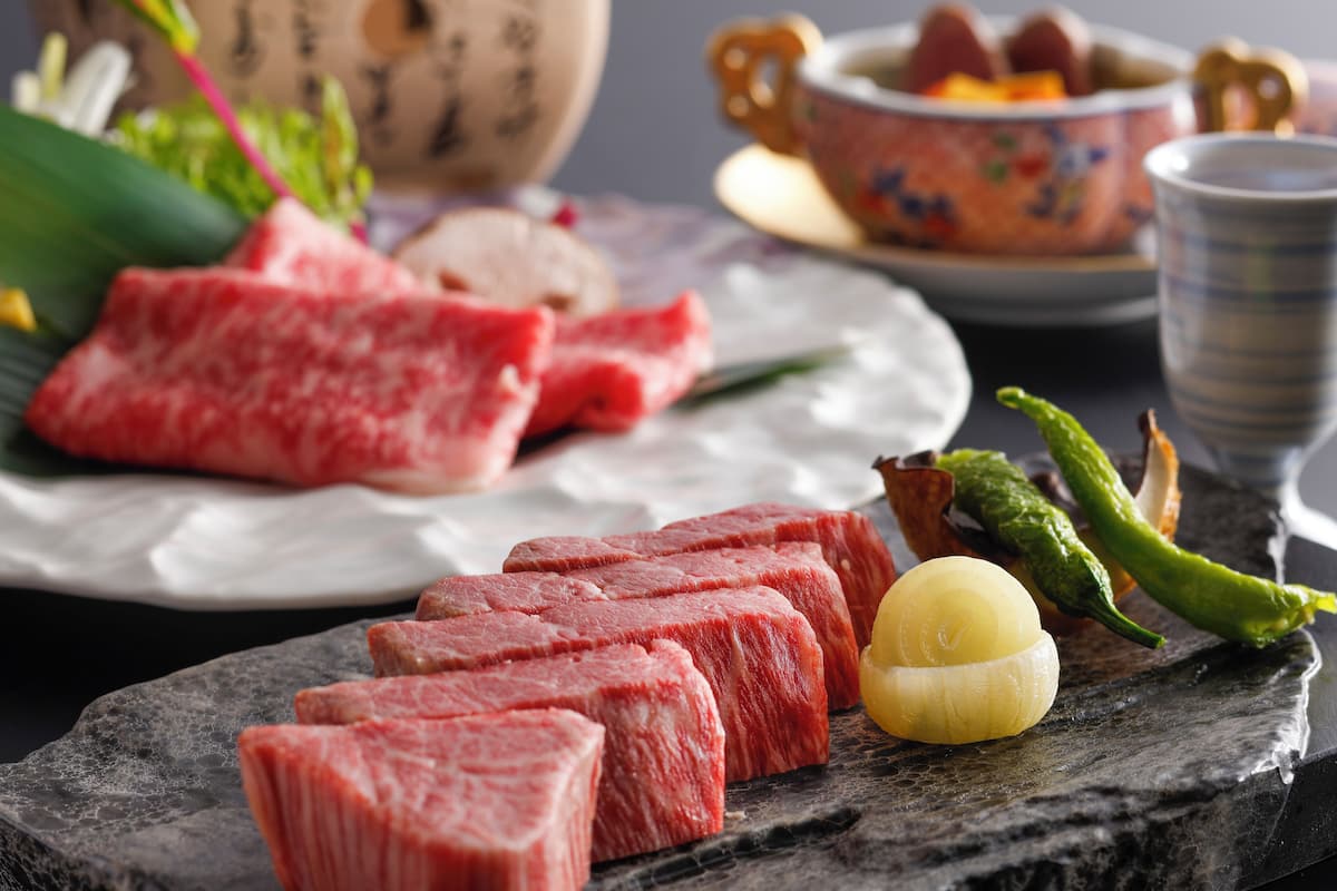 Ein Teller mit rohen Scheiben Rindfleisch und einer gelben Zwiebel auf einer Schieferplatte.