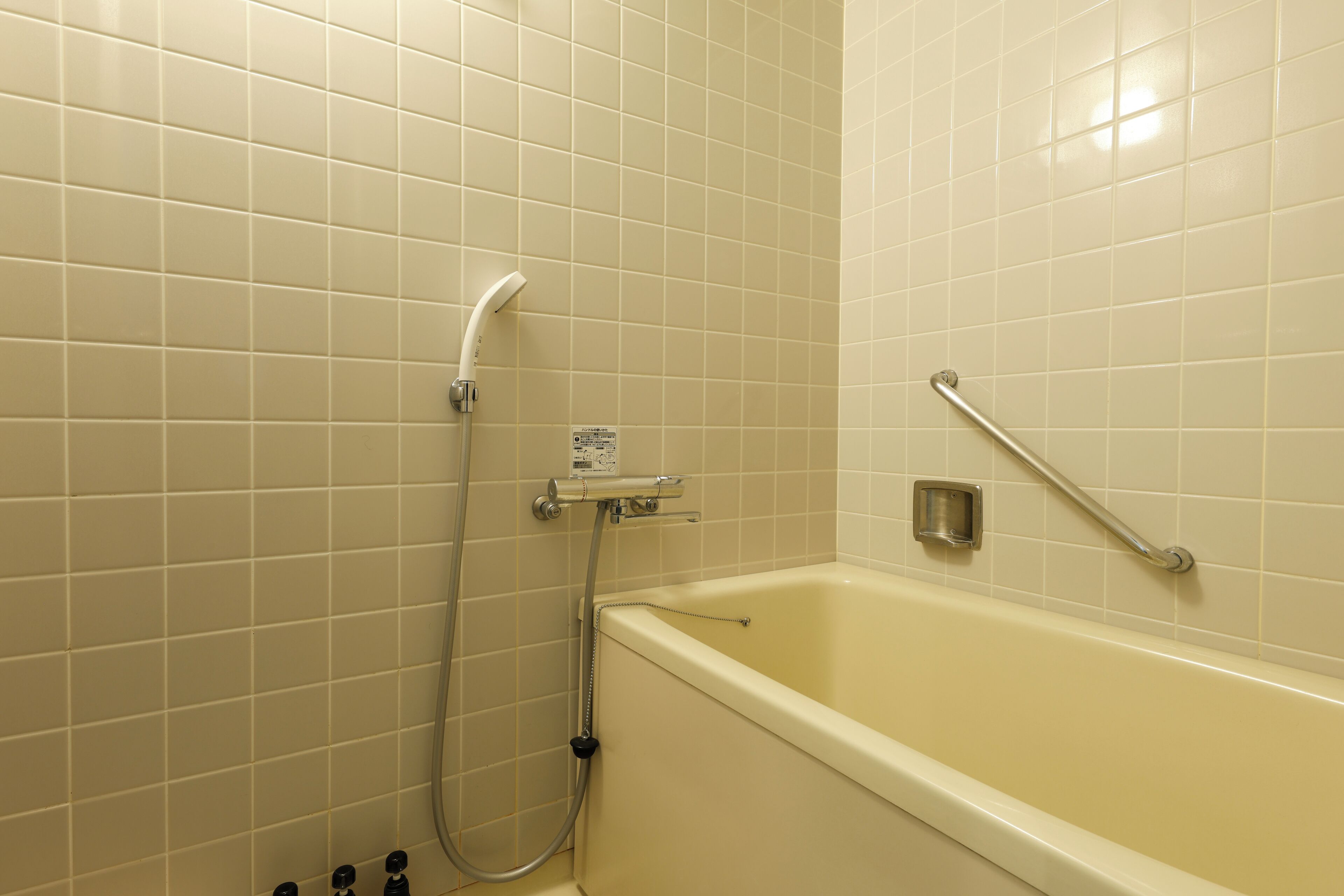 A bathroom with a bathtub, a handheld showerhead, and a grab bar.