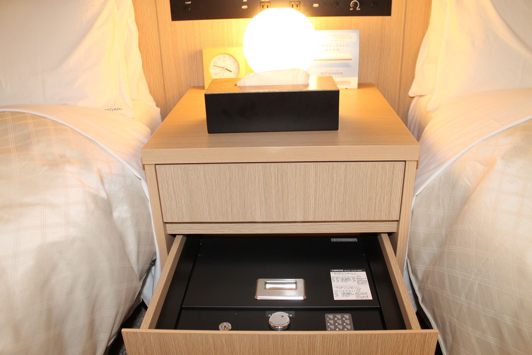 A wooden bedside table with a clock, a tissue box, and a drawer with a lock.