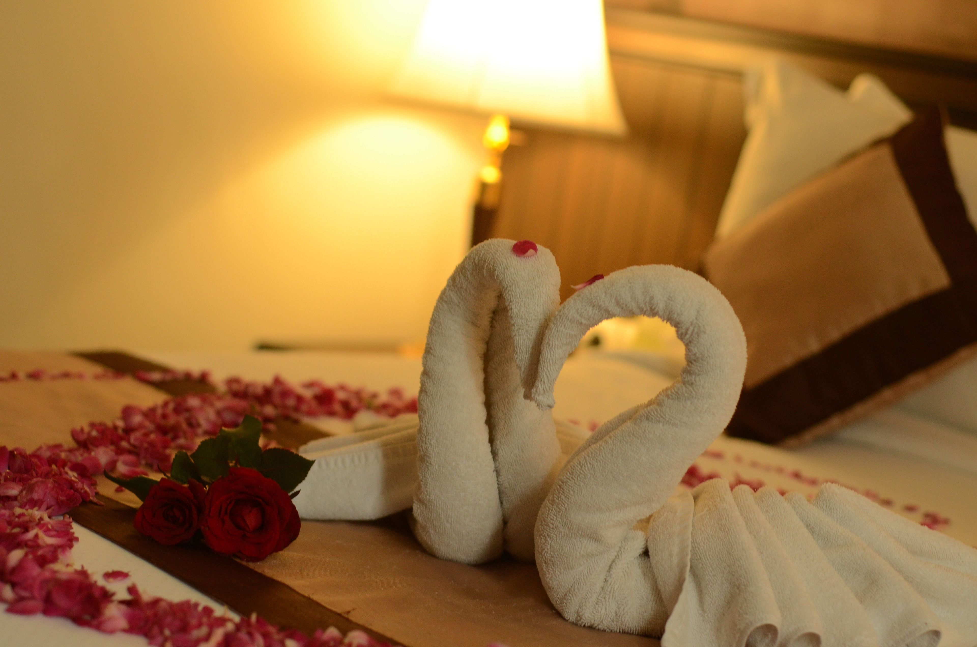 Una cama con cabecera de madera, almohada blanca y una decoración de toallas con forma de cisne.
