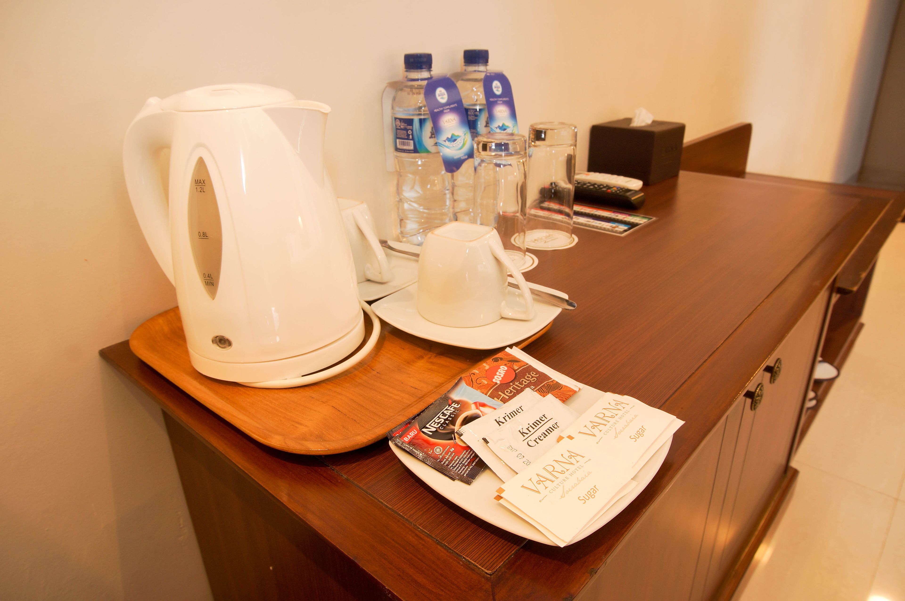 A hotel room's breakfast area with a coffee maker, water bottles, a tissue box, and a tray with coffee creamer packets.