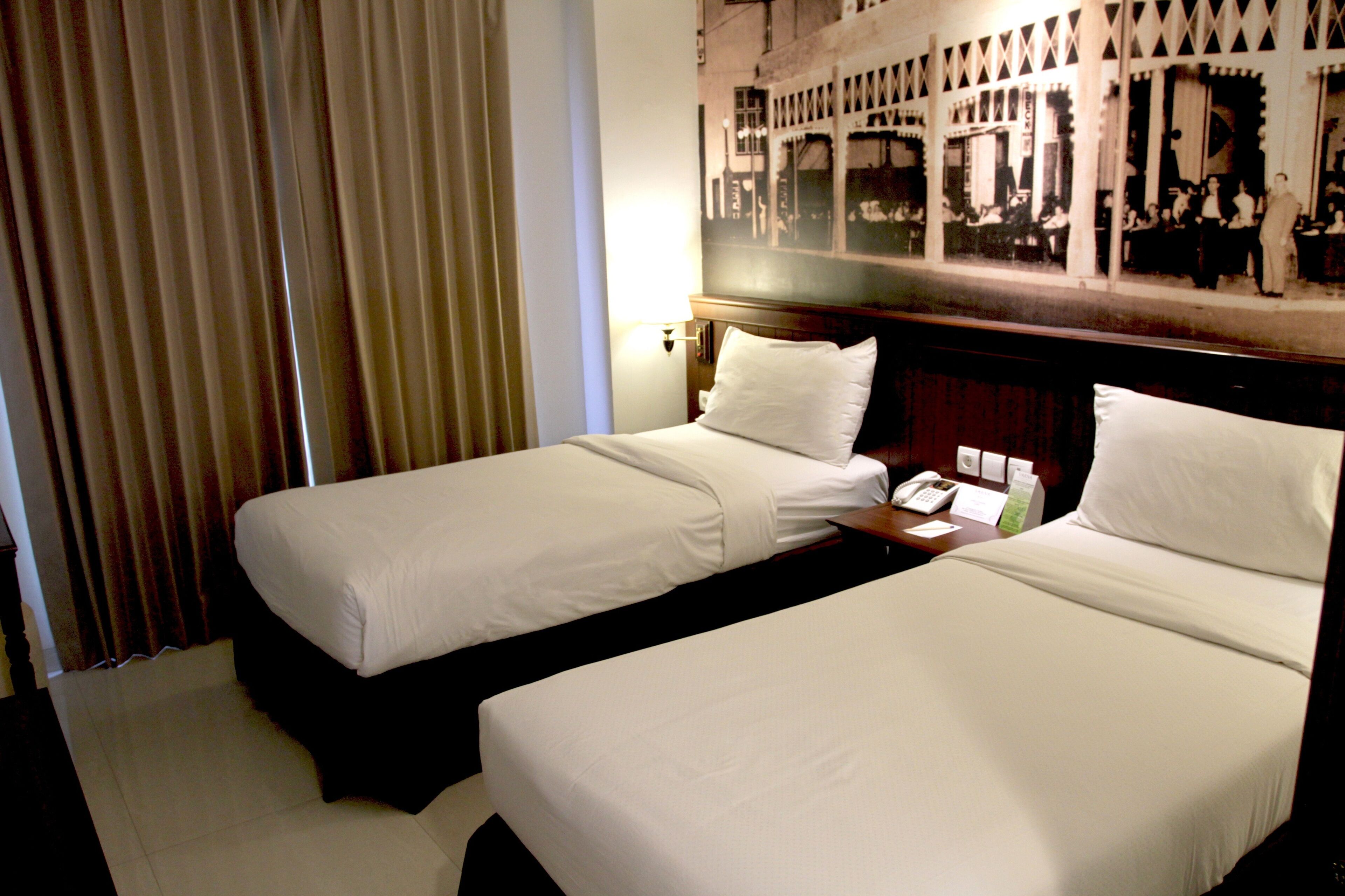 A hotel room with two single beds, a nightstand with a telephone, and a wall-mounted mirror.