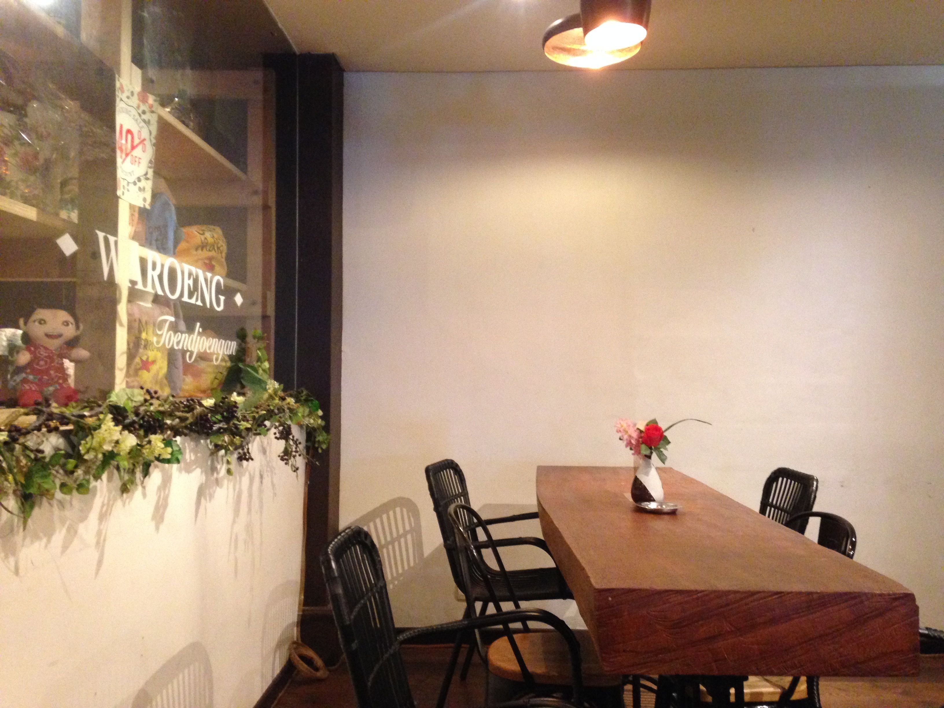 Un comedor con una mesa de madera y cuatro sillas, un jarrón con flores y una ventana con un letrero.