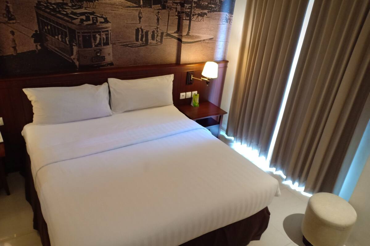 A hotel room with a large bed, a nightstand with a lamp, a small table, and a chair.