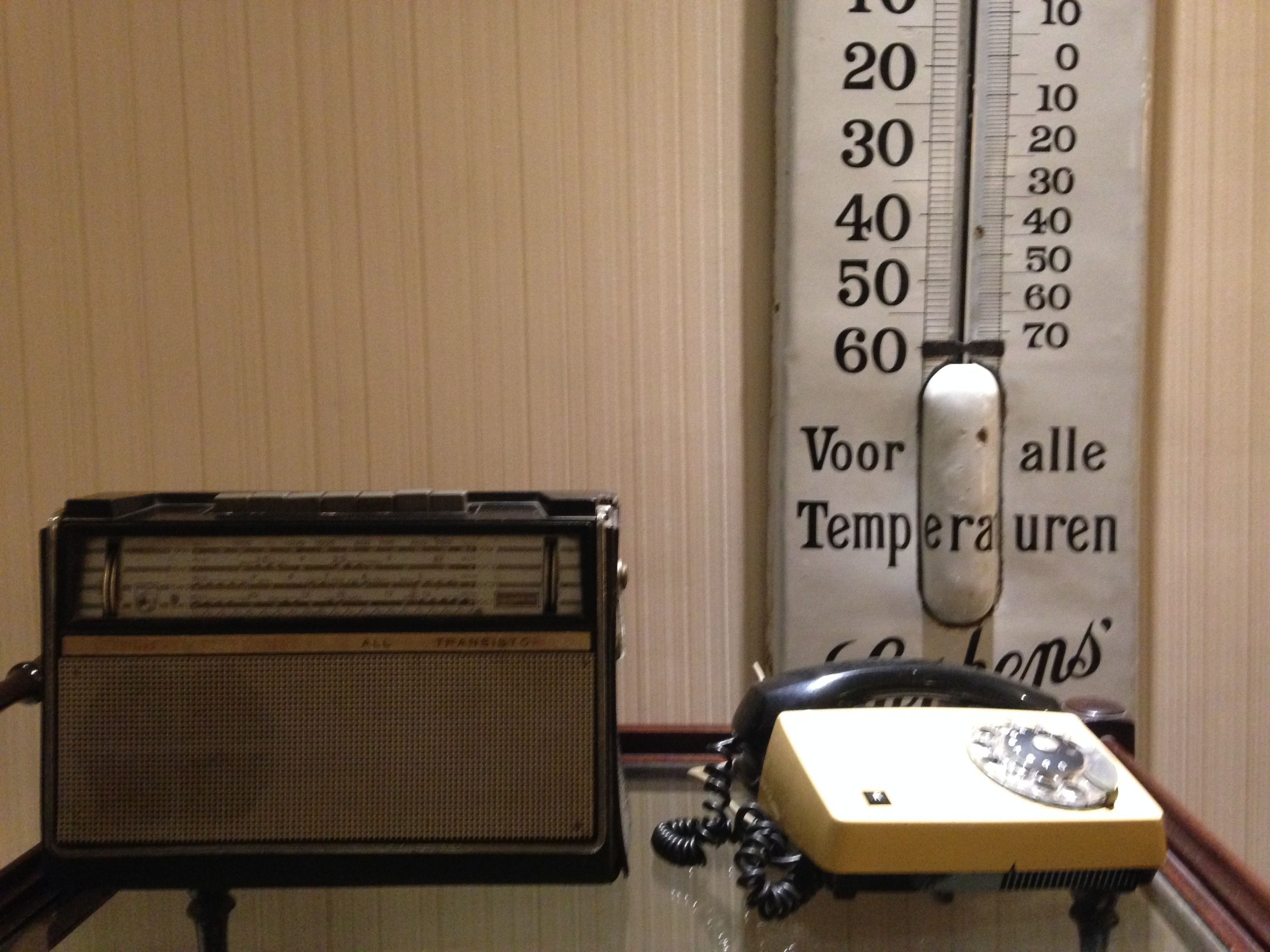 A vintage radio, a rotary dial telephone, and a thermometer on a table.