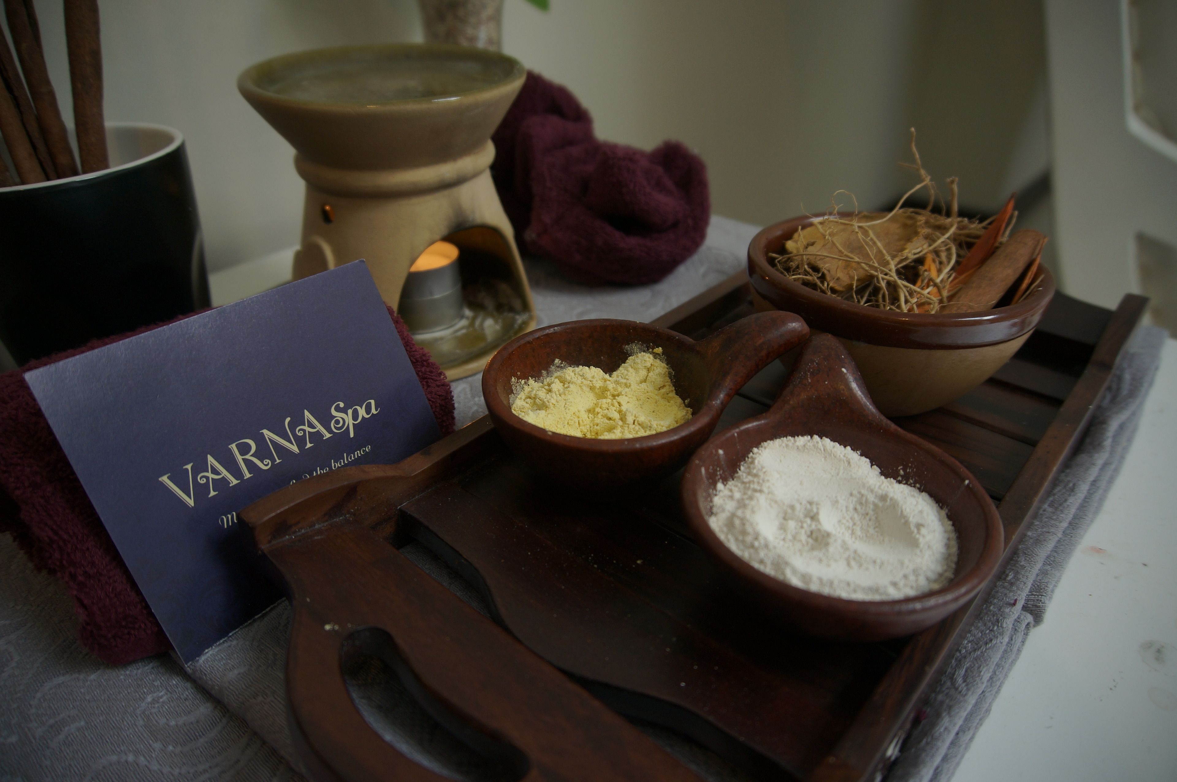 Un plateau contenant des bols remplis de poudres, une bougie et un livre intitulé « VARNA Spa ».