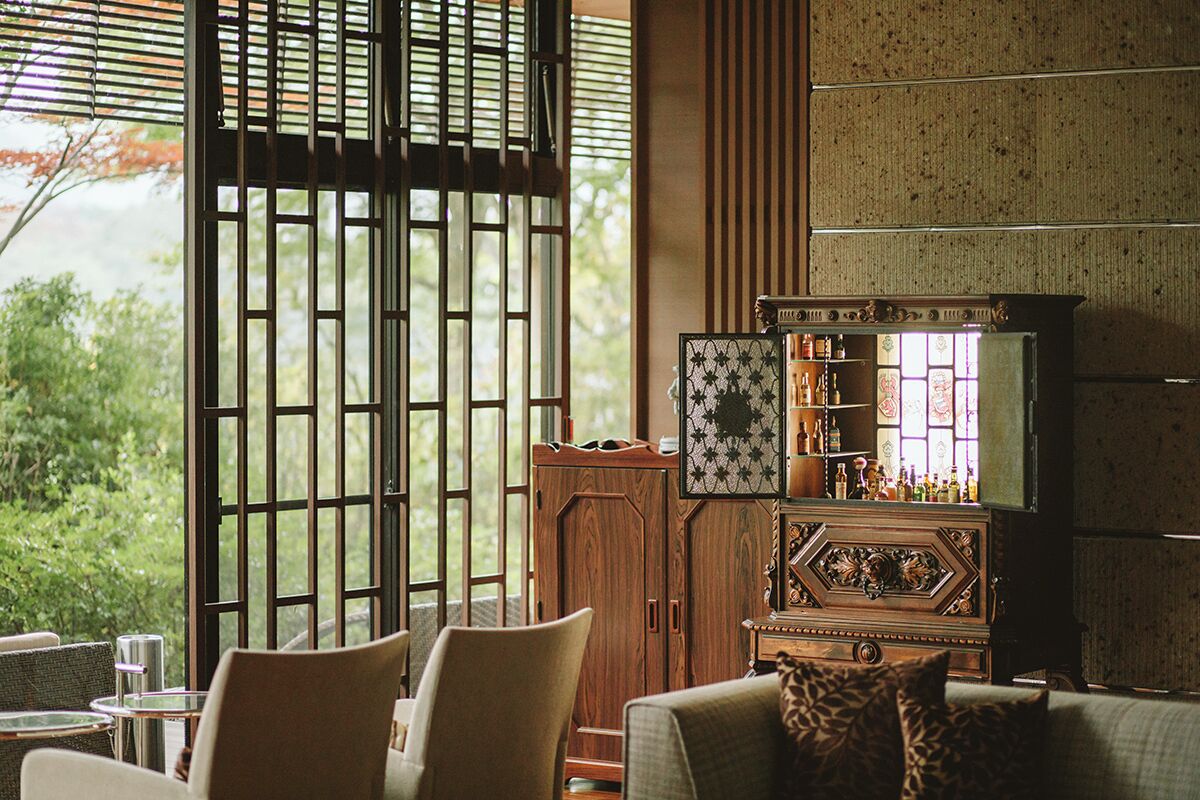 A room with a wooden cabinet, a sofa with patterned cushions, and a view of greenery outside.