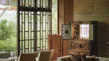 A room with a wooden cabinet, a sofa with patterned cushions, and a view of greenery outside.