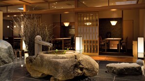 A traditional Japanese interior with tatami flooring, a stone water feature, and a sliding door with a view of the dining area. - Kinugawa Kanaya Hotel (Nikko)