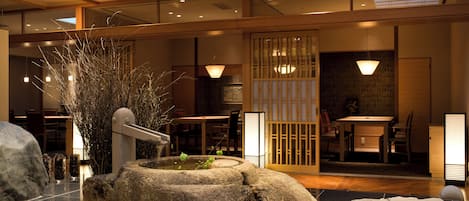 A traditional Japanese interior with tatami flooring, a stone water feature, and a sliding door with a view of the dining area.