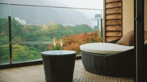 A balcony with a wicker sofa and a small table, two glasses of champagne, and a view of a mountainous landscape. - Kinugawa Kanaya Hotel (Nikko)