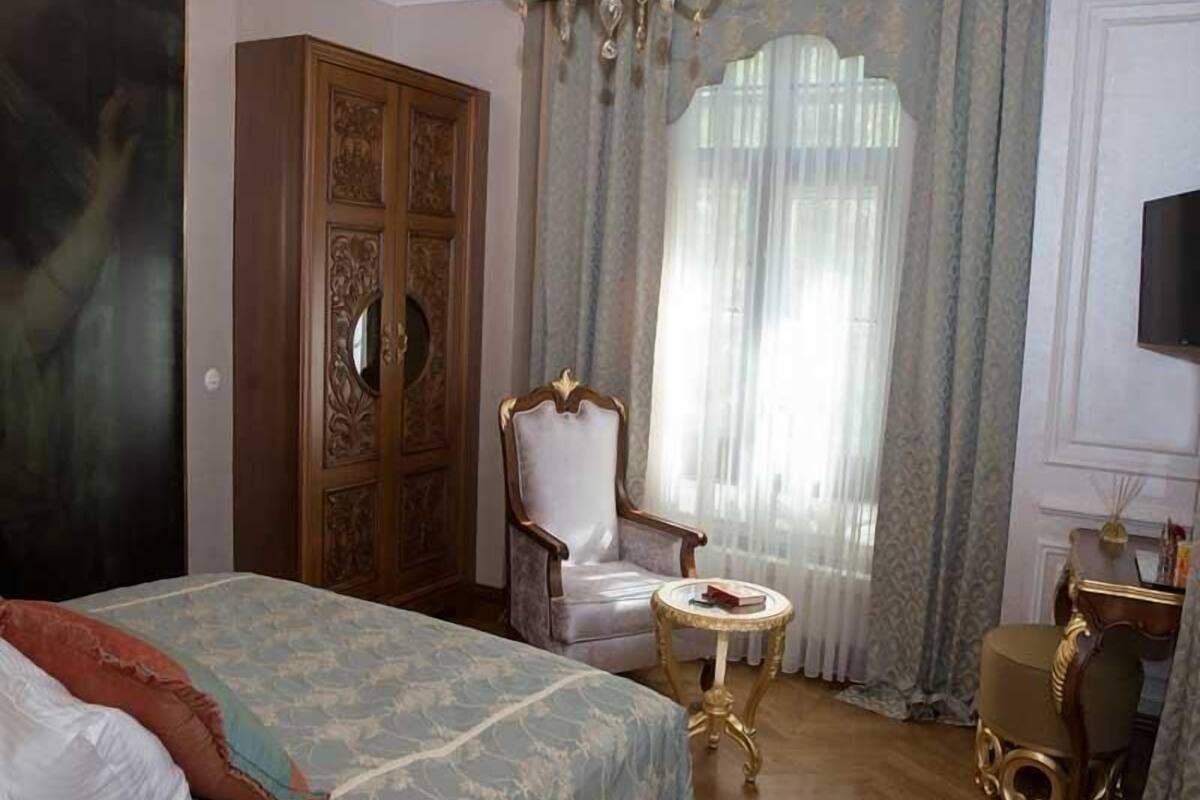 Un dormitorio con una cama grande, un armario, una silla, una mesita pequeña y un televisor en la pared.