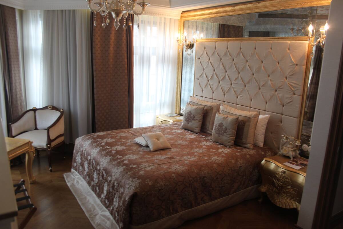 Un dormitorio amplio con una cama grande, una zona de estar con una silla y un espejo grande.