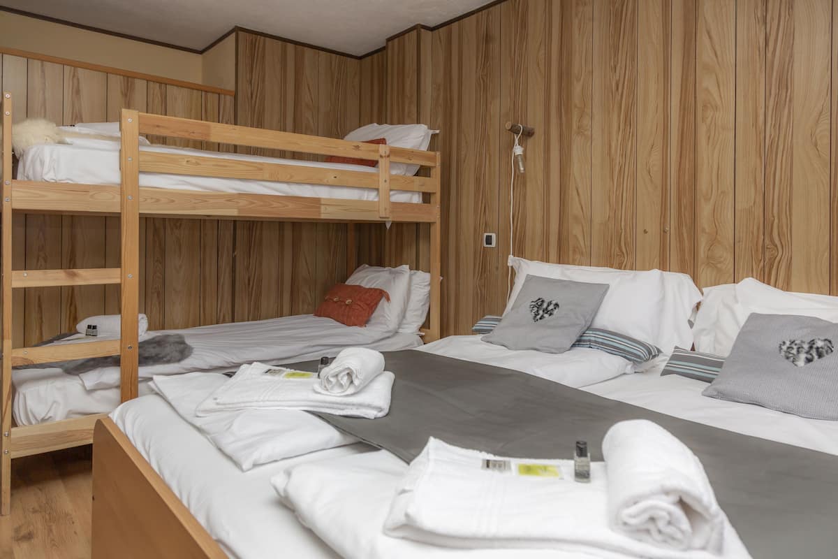 A bunk bed room with wooden walls, a single bed with white bedding, and a neatly made bed with towels.